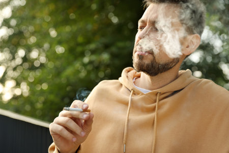 Handsome mature man smoking cigarette outdoors on sunny dayの写真素材