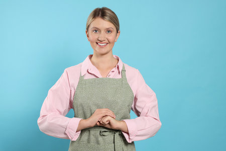 Beautiful young woman in clean apron with pattern on light blue backgroundの写真素材