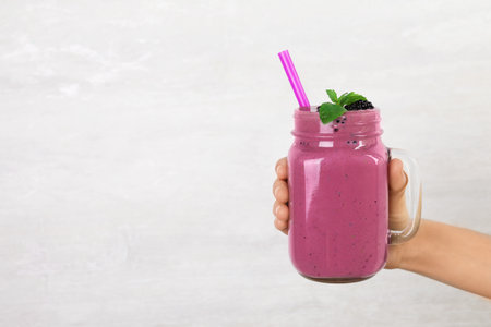Young woman holding mason jar of tasty blackberry smoothie on light gray background, closeup. Space for textの写真素材