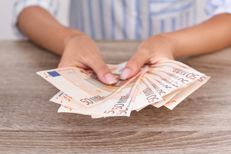 Woman with Euro banknotes at wooden table, closeupの写真素材