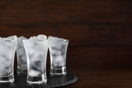 Shot glasses with vodka and ice on table against wooden background. Space for textの写真素材