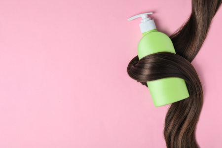 Shampoo bottle wrapped in lock of hair on pink background, flat lay with space for text. natural cosmetic productsの写真素材