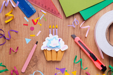 Paper cupcake, confetti and stationery on wooden table, flat layの写真素材