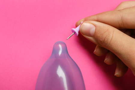 Woman piercing inflated condom with pin on pink background, closeup. safe sexの写真素材