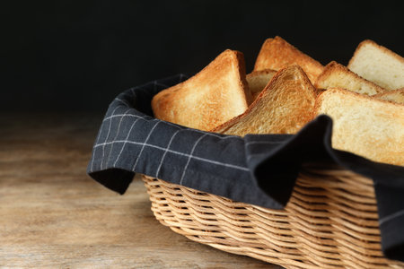 Slices of toasted bread in basket on wooden table against black backgroundの写真素材