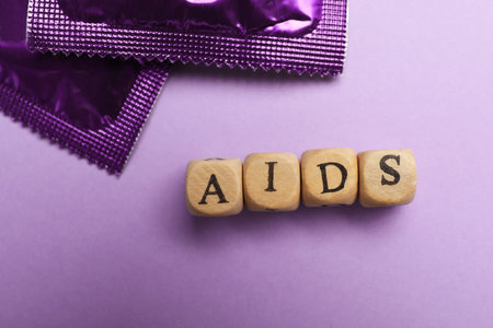 Condoms and word AIDS made with wooden cubes on violet background, flat lay. safe sexの写真素材