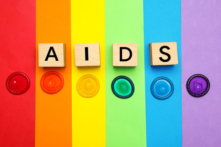 Word AIDS made with wooden cubes and colorful condoms on rainbow background, flat lay. safe sexの写真素材