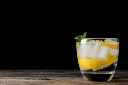Vodka cocktail with lemon and ice on wooden table against black background. Space for textの写真素材