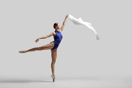 Graceful young ballerina practicing dance moves with veil on light gray backgroundの写真素材