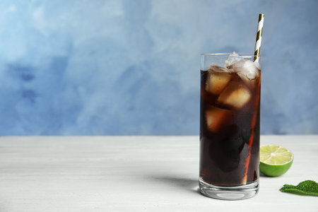Refreshing soda drink with ice cubes and lime on white wooden table against blue background, space for textの写真素材