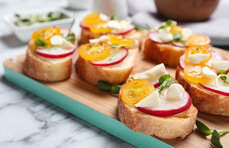 Tasty bruschettas with radish and yellow cherry tomatoes on white marble table, closeupの写真素材