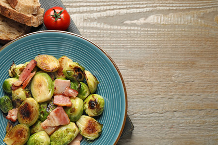 Delicious Brussels sprouts with bacon in plate on wooden table, flat lay. Space for textの写真素材