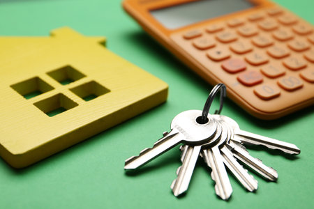 House figure with calculator and keys on green background, closeup. real estate agent serviceの写真素材