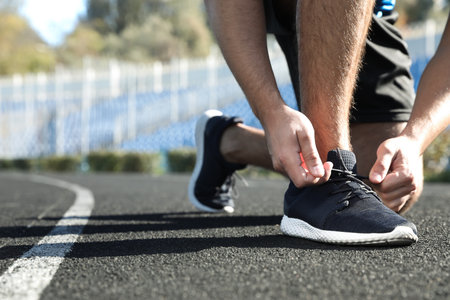 Sporty man tying shoelaces before running at stadiumの写真素材