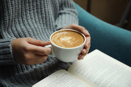 Woman with cup of coffee reading book at home, closeupの写真素材