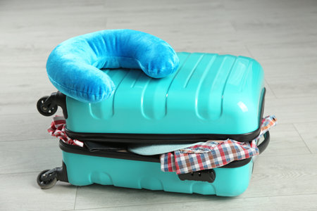 Suitcase with clothes and travel pillow on wooden floorの写真素材