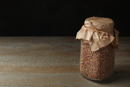 Buckwheat grains in jar on wooden table. Space for textの写真素材