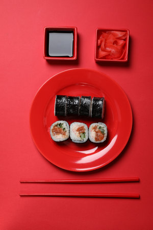 Tasty sushi rolls, soy sauce and ginger on red background, flat layの写真素材