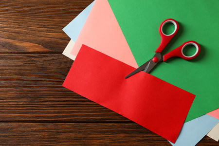 Red scissors and color paper on wooden table, flat lay. Space for textの写真素材