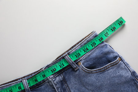 Jeans with measuring tape on light gray background, top view and space for text. weight loss conceptの写真素材