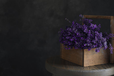 Beautiful lavender flowers in wooden basket on table against dark background. Space for textの写真素材