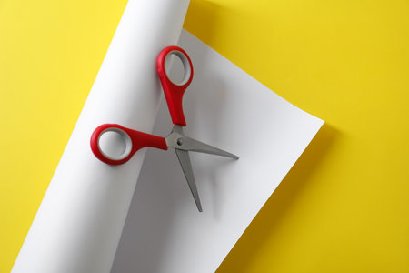 Red scissors and white paper on yellow background, top viewの写真素材