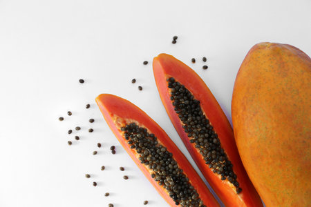 Fresh ripe cut and whole papaya fruits near scattered seeds on white background, flat lay. Space for textの写真素材