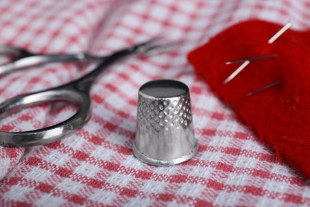 Silver thimble on checkered cloth, closeup. Sewing accessoryの写真素材