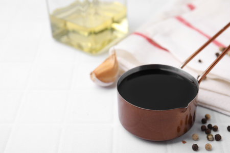 Metal small saucepan with balsamic vinegar and ingredients on white tiled table. Space for textの写真素材