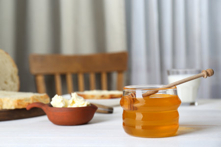 Jar with honey, butter, bread and milk served for breakfast on white wooden tableの写真素材