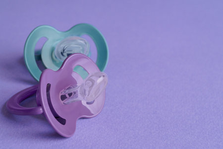 New baby pacifiers on purple background, closeup. Space for textの写真素材