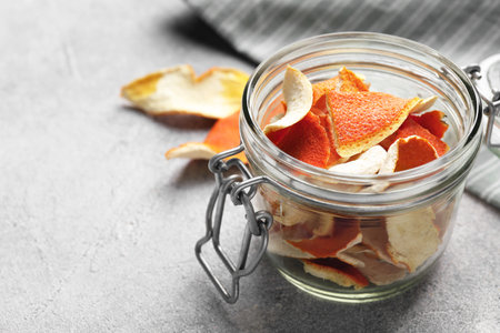 Glass jar with dry orange peels on light gray textured table, space for textの写真素材