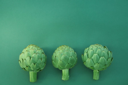 Whole fresh raw artichokes on green background, flat lay. Space for textの写真素材