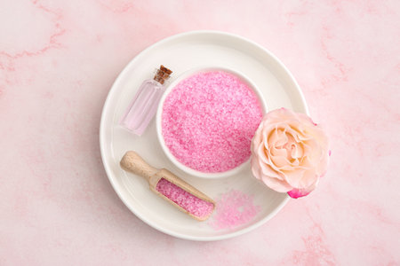 Bowl and scoop with sea salt, beautiful rose on pink marble table, top viewの写真素材