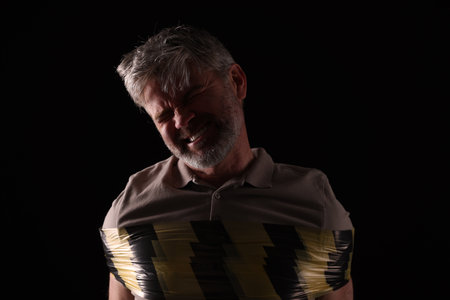 Emotional victim tied with duct tape on black background. Hostage takingの写真素材