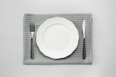 Clean plate and shiny silver cutlery on light gray background, flat layの写真素材