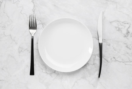 Clean plate and shiny silver cutlery on white marble table, flat layの写真素材