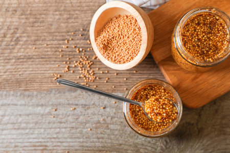 Bowl and jars of whole grain mustard on wooden table, flat lay. Space for textの写真素材