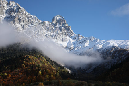 Picturesque landscape of high mountains covered with thick mist under blue sky on autumn day