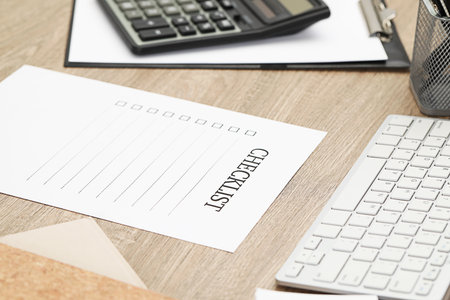 Sheet of paper with inscription Checklist on wooden table at workplace