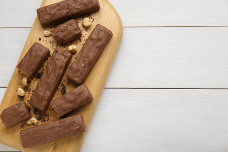Board with delicious chocolate bars and nuts on white wooden table, top view. Space for textの写真素材