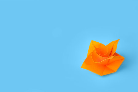 origami art. Handmade orange paper flower on light blue background, space for textの写真素材