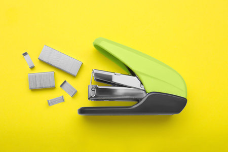 New bright stapler with staples on yellow background, fat lay. school stationeryの写真素材