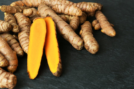 Whole and cut turmeric roots on black textured table, closeupの写真素材