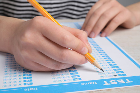 Student filling answer sheet at table, closeup. Passing exam