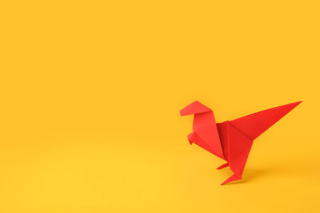 origami art. Handmade red paper dinosaur on yellow background, space for textの写真素材