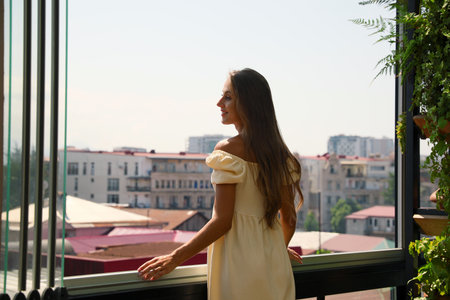 Beautiful young woman with long hair standing on balconyの写真素材