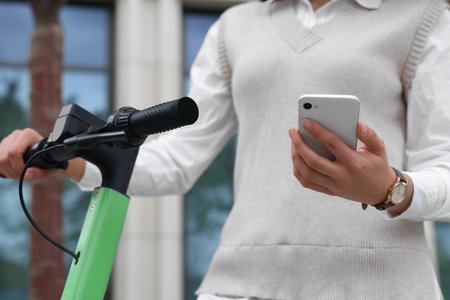 Businesswoman with modern kick scooter using smartphone on city street, closeupの写真素材