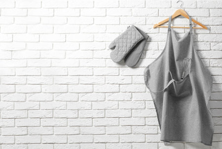 Clean kitchen apron with pattern and oven gloves on white brick wall. Space for textの写真素材