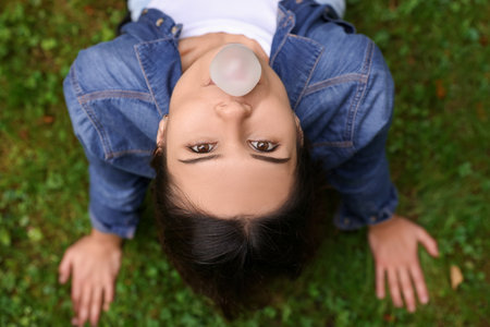 Beautiful young woman blowing chewing gum on green grass outdoors, top viewの写真素材